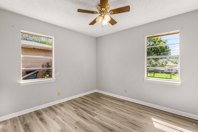 empty room featuring ceiling fan, a healthy amount of sunlight, a textured ceiling, and light wood-type flooring