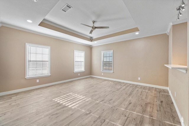 empty room with crown molding, light wood-type flooring, and a tray ceiling