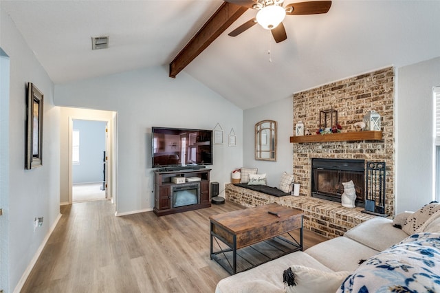 living room with lofted ceiling with beams, ceiling fan, a brick fireplace, and light wood-type flooring