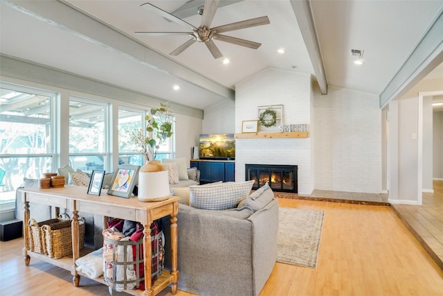 living room with ceiling fan, a fireplace, light hardwood / wood-style floors, and vaulted ceiling with beams