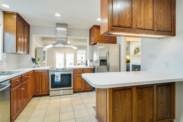 kitchen featuring appliances with stainless steel finishes, island range hood, tasteful backsplash, light tile patterned floors, and kitchen peninsula