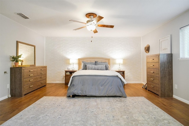 bedroom featuring hardwood / wood-style flooring, ceiling fan, and brick wall