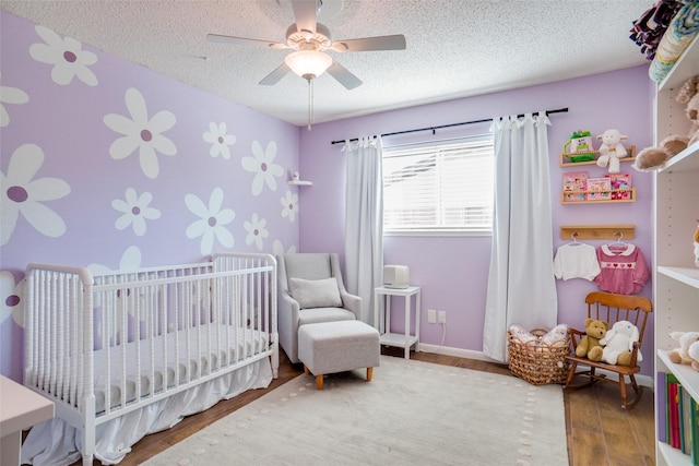 bedroom with ceiling fan, hardwood / wood-style floors, a textured ceiling, and a crib