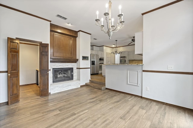 kitchen with light stone counters, stainless steel appliances, a stone fireplace, and light hardwood / wood-style flooring