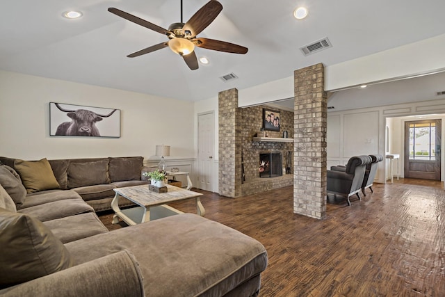 living room with ceiling fan, dark hardwood / wood-style floors, decorative columns, and a brick fireplace