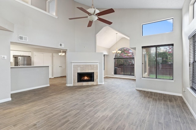 unfurnished living room featuring a tiled fireplace, ceiling fan with notable chandelier, and a high ceiling