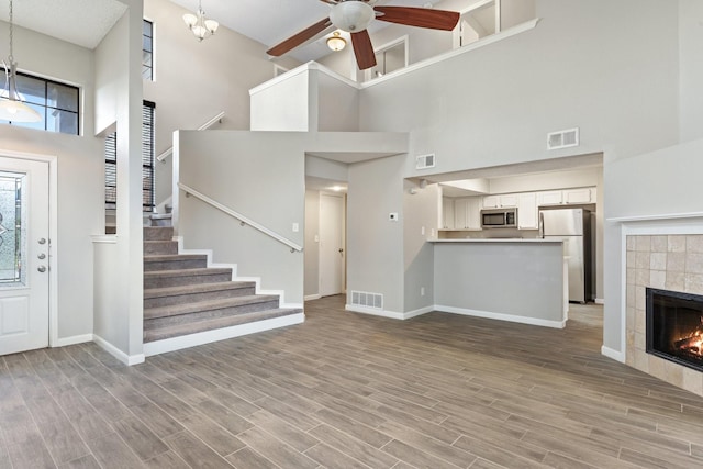 unfurnished living room featuring ceiling fan, a towering ceiling, a fireplace, and light hardwood / wood-style floors