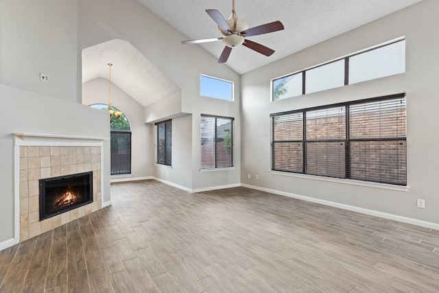 unfurnished living room featuring a tiled fireplace, a towering ceiling, a textured ceiling, and ceiling fan