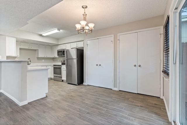 kitchen with white cabinetry, appliances with stainless steel finishes, decorative light fixtures, and a textured ceiling