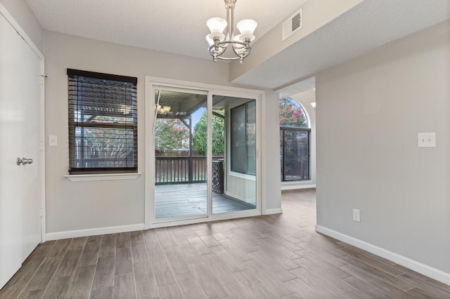 spare room featuring wood-type flooring, a notable chandelier, and a textured ceiling