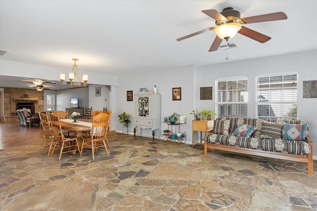 dining area featuring ceiling fan with notable chandelier and a large fireplace