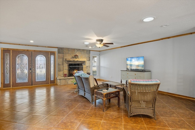 living room featuring crown molding, a stone fireplace, ceiling fan, and french doors