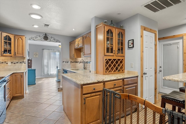 kitchen featuring light tile patterned flooring, sink, kitchen peninsula, light stone countertops, and decorative backsplash