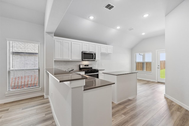 kitchen with stainless steel appliances, light hardwood / wood-style floors, white cabinets, vaulted ceiling, and kitchen peninsula