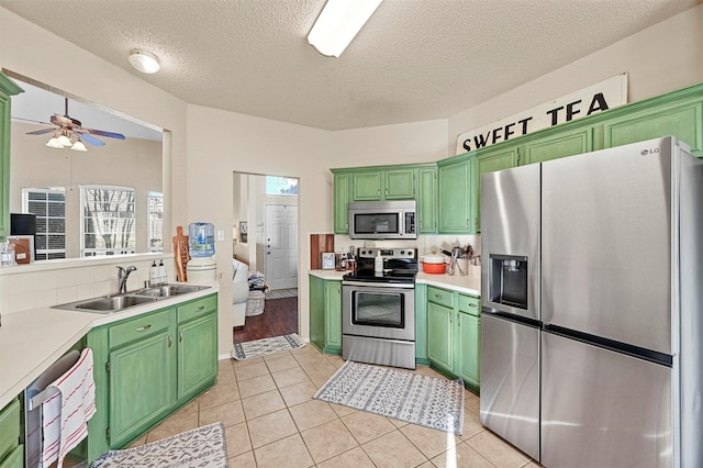 kitchen with tasteful backsplash, sink, green cabinets, light tile patterned floors, and stainless steel appliances