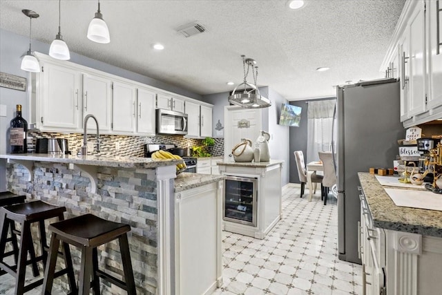 kitchen with pendant lighting, appliances with stainless steel finishes, a kitchen breakfast bar, and white cabinets