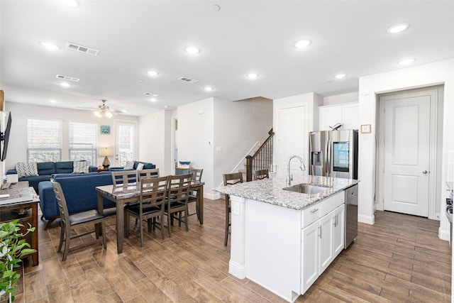 kitchen featuring appliances with stainless steel finishes, light stone countertops, a kitchen island with sink, and white cabinets