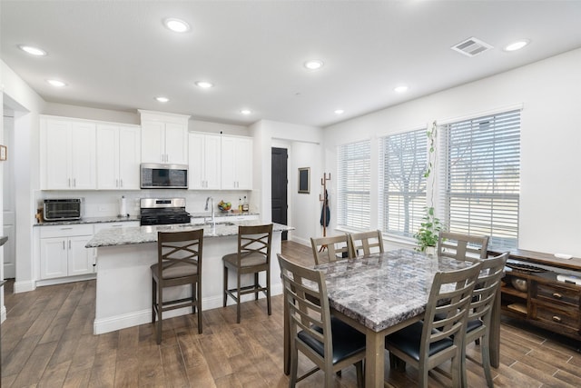 kitchen with a breakfast bar area, white cabinetry, stainless steel appliances, light stone countertops, and an island with sink