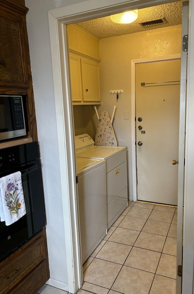 washroom featuring washing machine and dryer, cabinets, and light tile patterned flooring