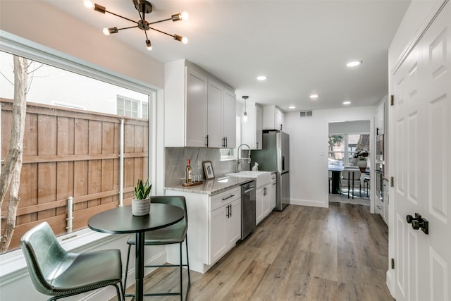 kitchen featuring white cabinetry, tasteful backsplash, light stone counters, light hardwood / wood-style flooring, and stainless steel appliances