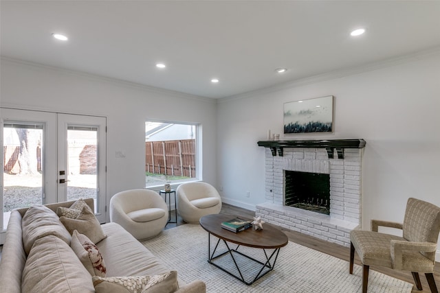 living room featuring a brick fireplace, crown molding, light hardwood / wood-style floors, and french doors