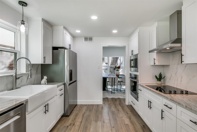 kitchen with wall chimney exhaust hood, sink, light stone counters, stainless steel appliances, and white cabinets