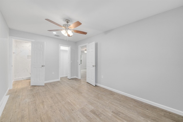 unfurnished bedroom with ensuite bath, a walk in closet, ceiling fan, light wood-type flooring, and a closet