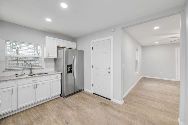 kitchen with sink, white cabinetry, light stone countertops, light hardwood / wood-style floors, and stainless steel fridge with ice dispenser