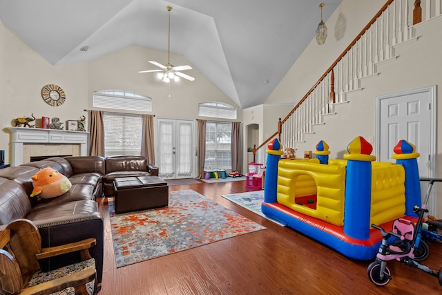 recreation room featuring a tile fireplace, high vaulted ceiling, hardwood / wood-style flooring, ceiling fan, and french doors