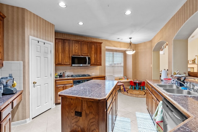 kitchen with sink, appliances with stainless steel finishes, decorative backsplash, a kitchen island, and decorative light fixtures