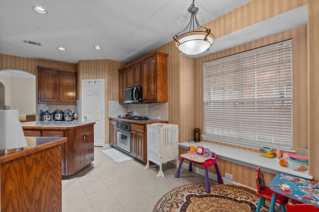 kitchen with tasteful backsplash, appliances with stainless steel finishes, decorative light fixtures, and light tile patterned flooring