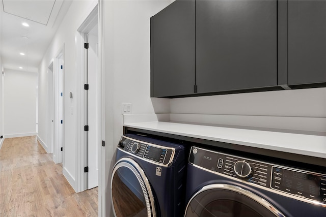 clothes washing area with cabinets, washing machine and dryer, and light hardwood / wood-style flooring