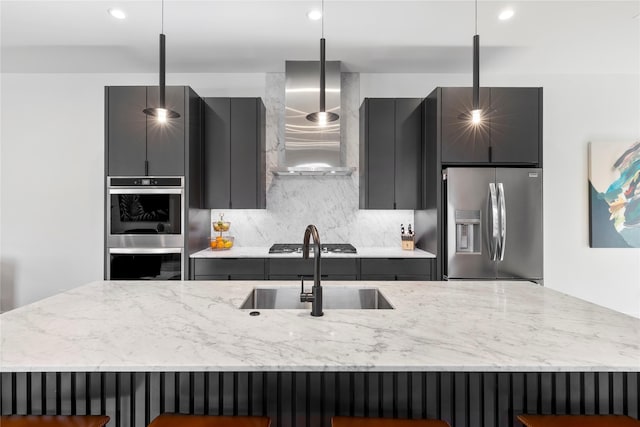 kitchen featuring pendant lighting, sink, a kitchen bar, stainless steel appliances, and wall chimney range hood