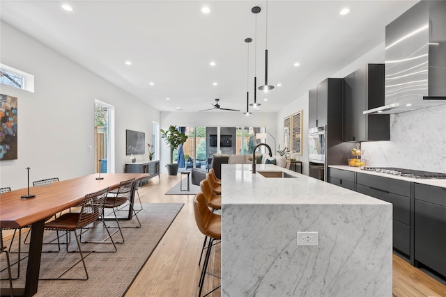 kitchen featuring extractor fan, pendant lighting, sink, decorative backsplash, and a center island with sink