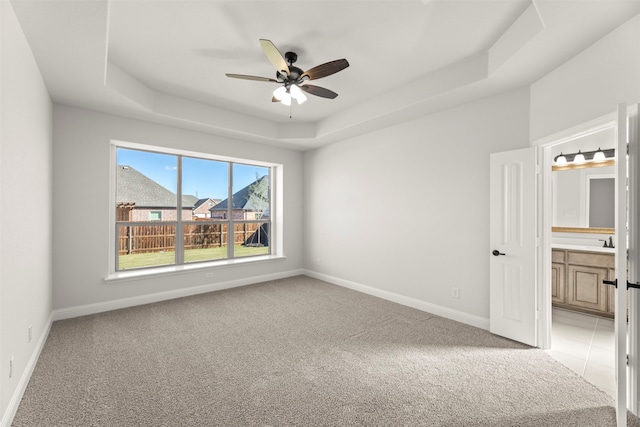 empty room with light colored carpet, ceiling fan, and a tray ceiling