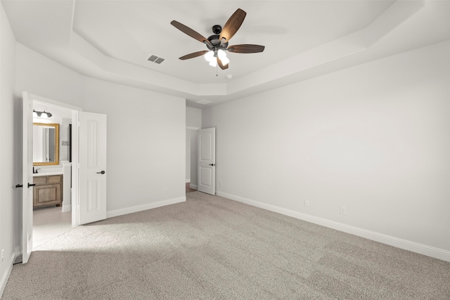 unfurnished bedroom with ceiling fan, light colored carpet, connected bathroom, and a raised ceiling