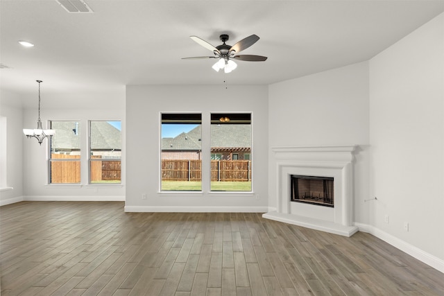 unfurnished living room with ceiling fan with notable chandelier, hardwood / wood-style floors, and a wealth of natural light