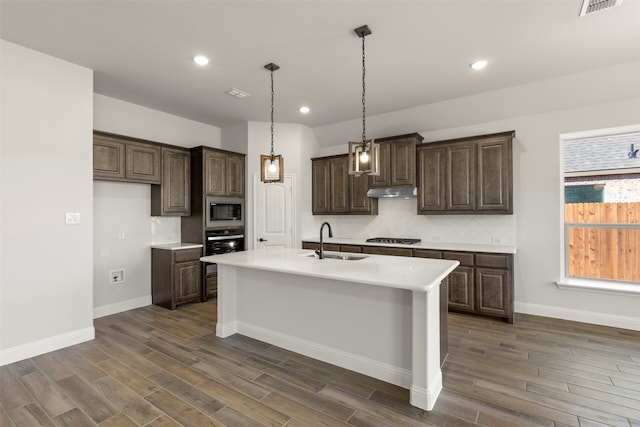 kitchen with stainless steel microwave, sink, oven, black gas stovetop, and a center island with sink