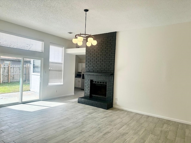 unfurnished living room featuring a notable chandelier, light hardwood / wood-style floors, a brick fireplace, and a textured ceiling