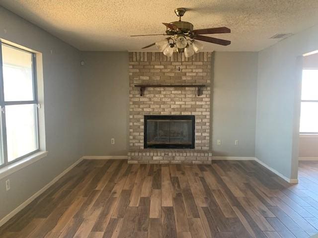 unfurnished living room featuring ceiling fan, a fireplace, dark hardwood / wood-style flooring, and a textured ceiling