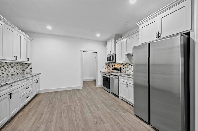 kitchen with stainless steel appliances, white cabinets, and light stone counters