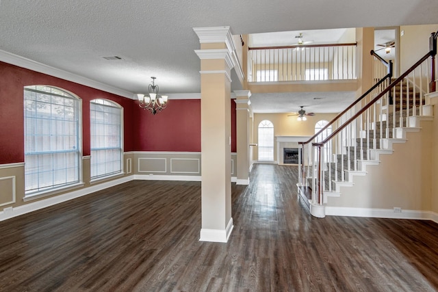 entryway featuring ceiling fan with notable chandelier, dark wood-type flooring, ornamental molding, and ornate columns