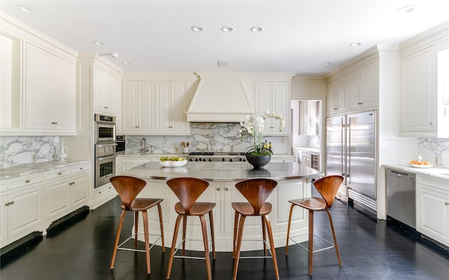 kitchen featuring premium range hood, appliances with stainless steel finishes, a breakfast bar area, and a kitchen island