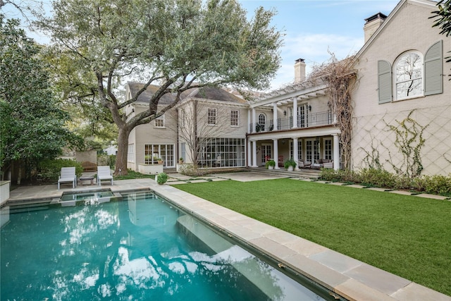 back of house featuring a balcony, a pergola, a patio area, and a lawn