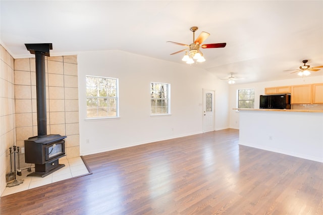 living room with lofted ceiling, a wealth of natural light, light hardwood / wood-style flooring, and a wood stove