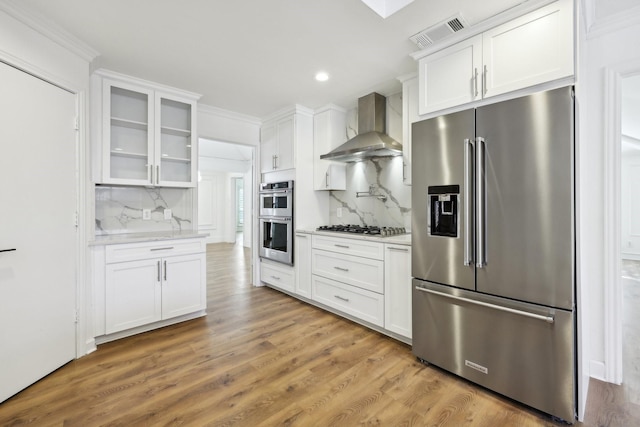 kitchen with stainless steel appliances, white cabinets, decorative backsplash, and wall chimney exhaust hood