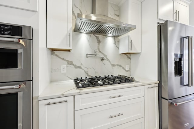 kitchen with appliances with stainless steel finishes, tasteful backsplash, white cabinetry, light stone counters, and wall chimney range hood