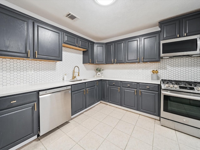 kitchen featuring sink, decorative backsplash, light tile patterned floors, stainless steel appliances, and a textured ceiling