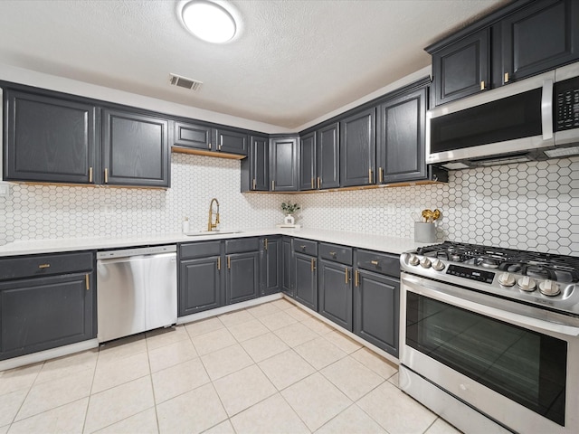 kitchen with light tile patterned floors, sink, appliances with stainless steel finishes, backsplash, and a textured ceiling