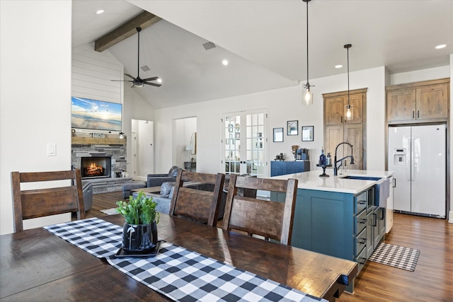 dining room featuring high vaulted ceiling, dark hardwood / wood-style floors, beamed ceiling, ceiling fan, and a fireplace